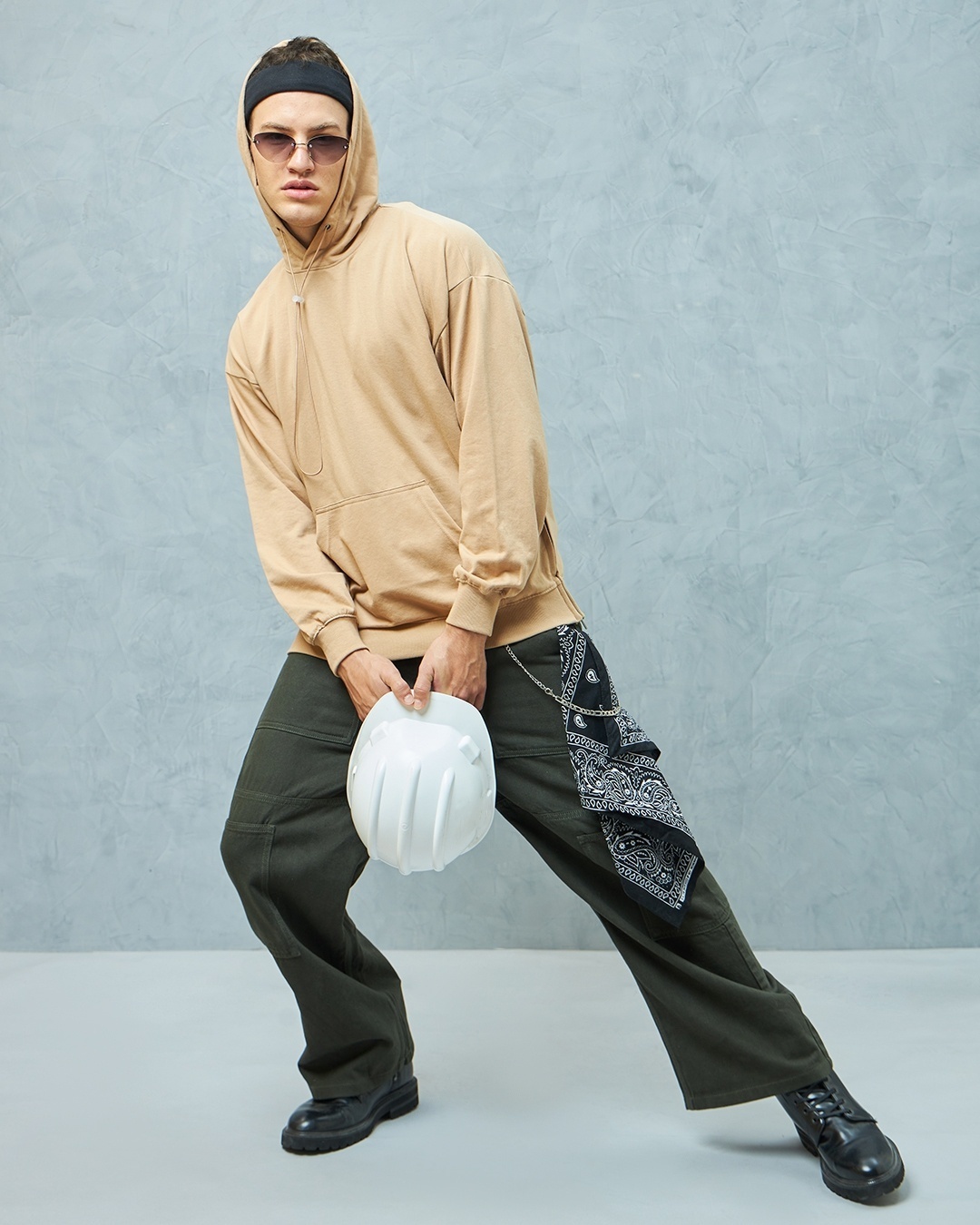 man giving a relax pos with a brown hoodie and black pant further styled with white cap